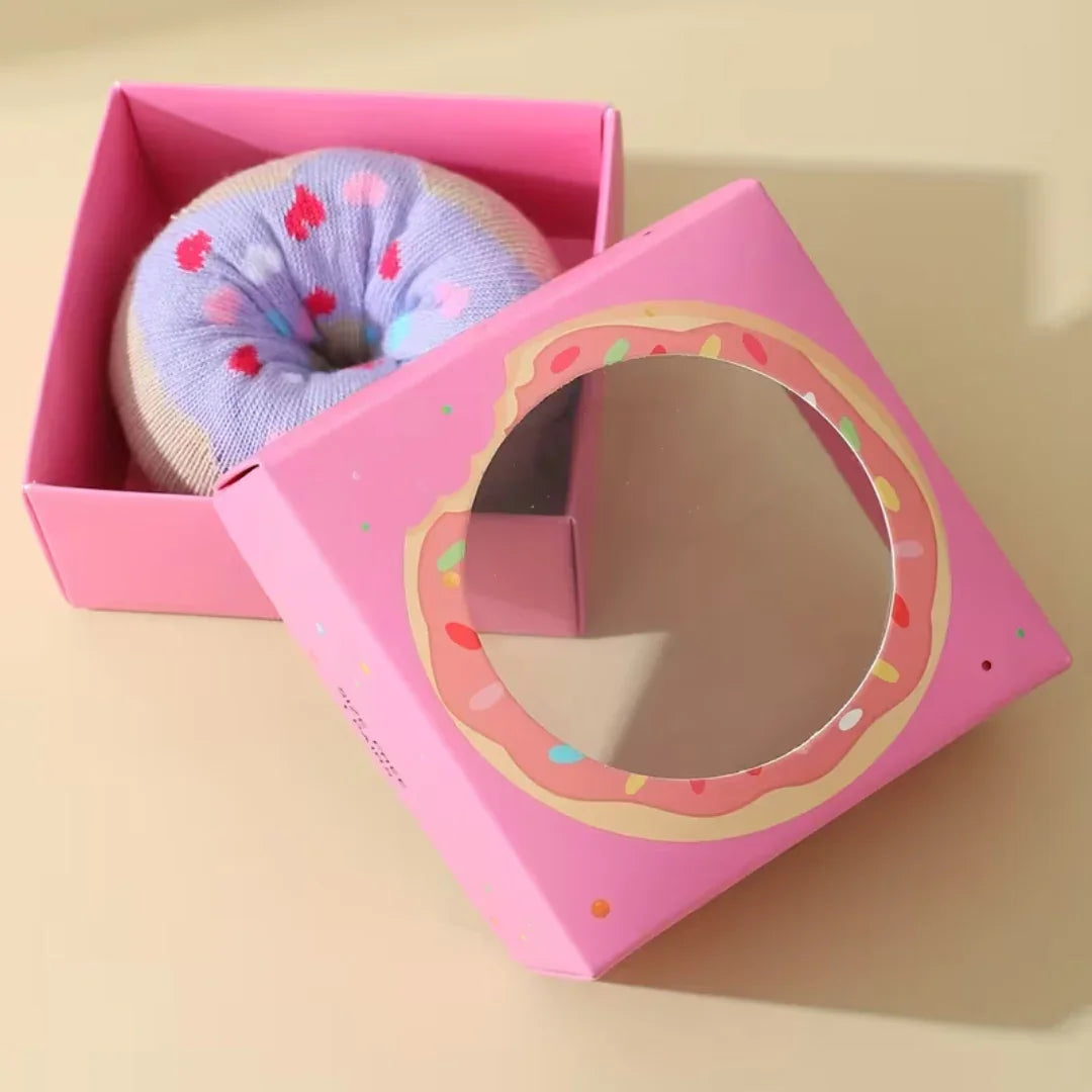 Fun donut-shaped cozy socks with colorful sprinkles inside a pink box with a donut design window
